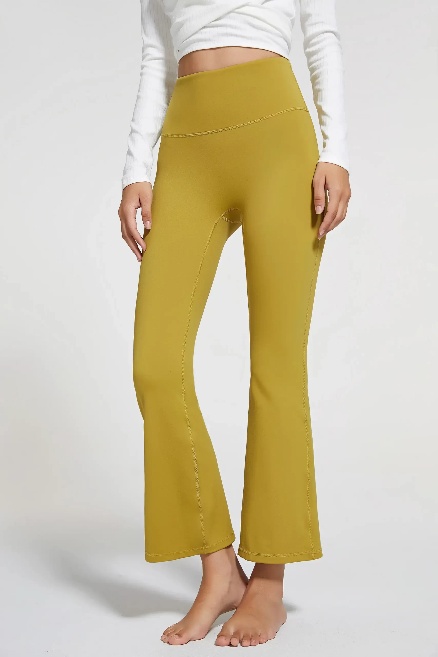 Close-up of a woman wearing mustard yellow flared yoga pants with a white long-sleeve top.