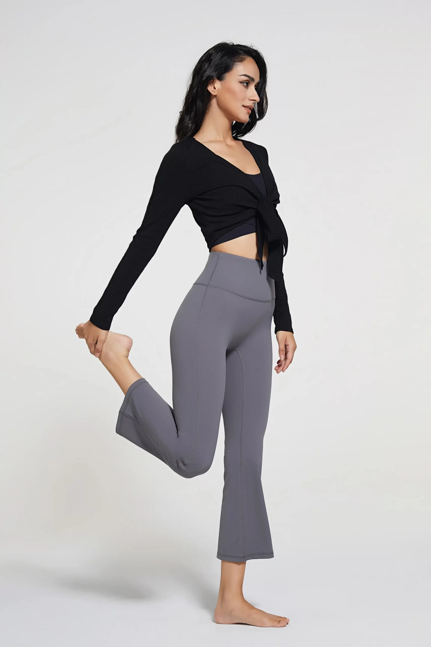 Woman wearing gray flared yoga pants paired with a black long-sleeve cropped top, stretching her leg.