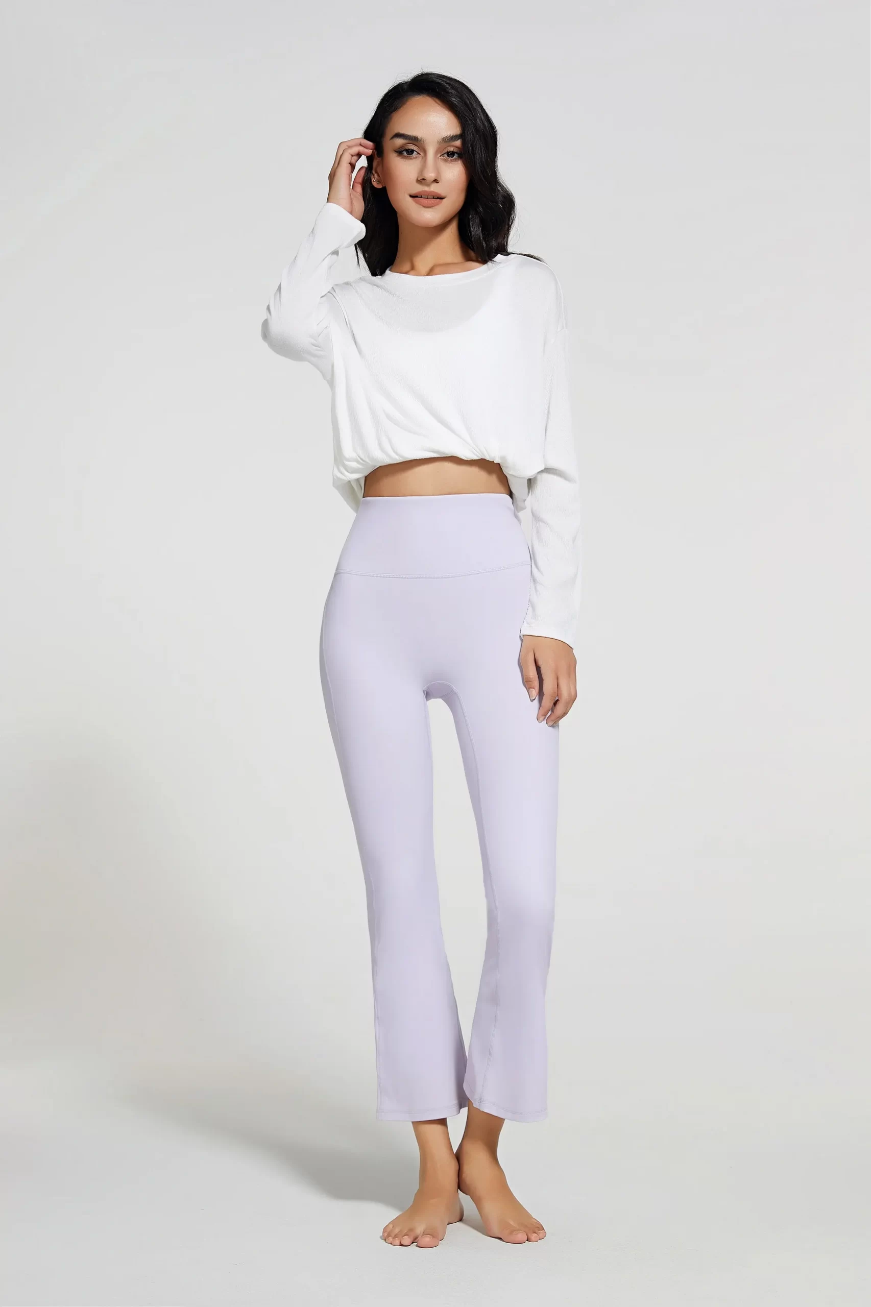 Woman wearing light purple flared yoga pants paired with a white cropped long-sleeve top.