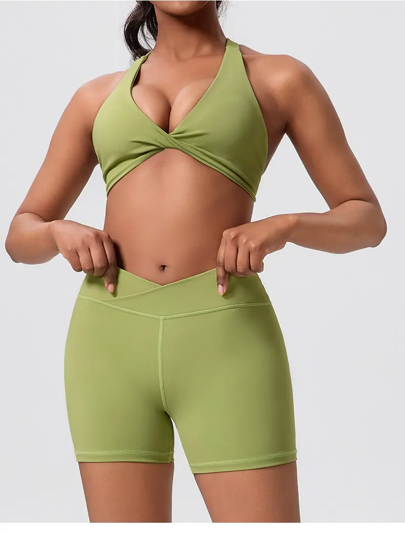 Woman wearing an olive green halter sports bra and matching high-waisted shorts, adjusting her waistband.