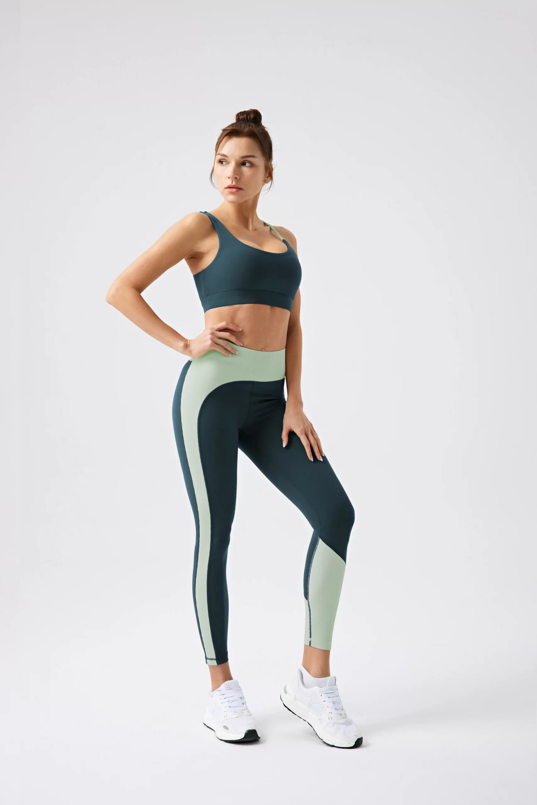 Woman in a teal and mint green color-blocked sports bra and matching leggings, standing confidently.