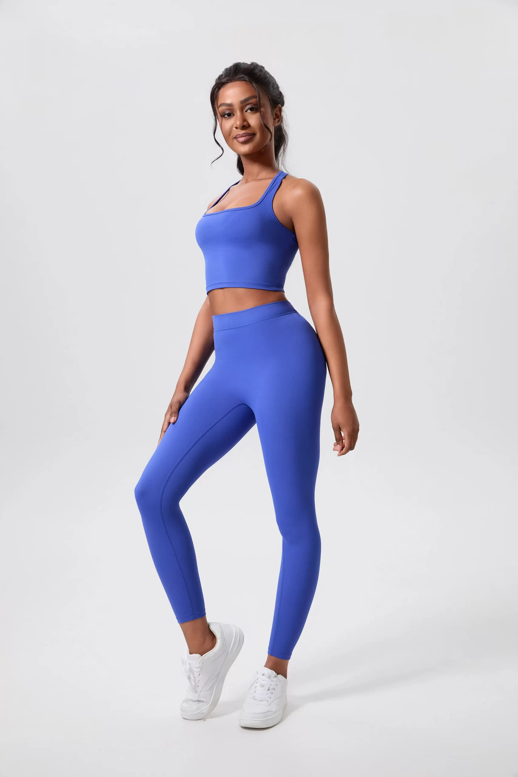 Woman in a vibrant blue sports bra and leggings set, standing confidently in white sneakers.